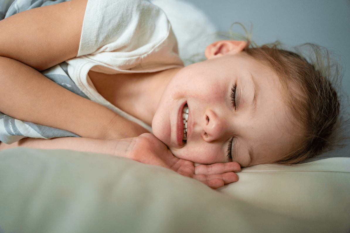 Primo piano di una bambina sdraiata nel letto che digrigna o serra i denti mentre dorme.