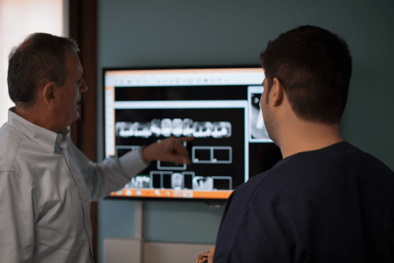 Dentista mostra e spiega una radiografia panoramica dentale su schermo a un paziente.