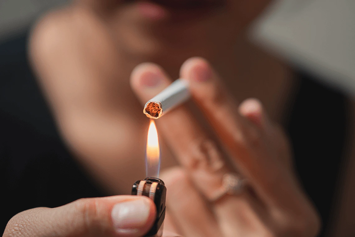 Primo piano di una persona che accende una sigaretta con la fiamma di un accendino.