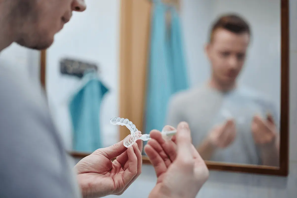 Ragazzo davanti allo specchio del bagno mentre applica un gel con una siringa all'interno di una mascherina trasparente o allineatore invisibile.