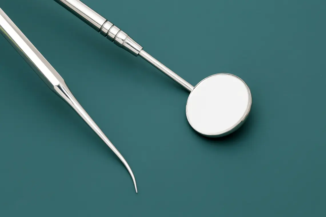 Specchietto e sonda dentistica in acciaio inox appoggiati su una superficie verde.