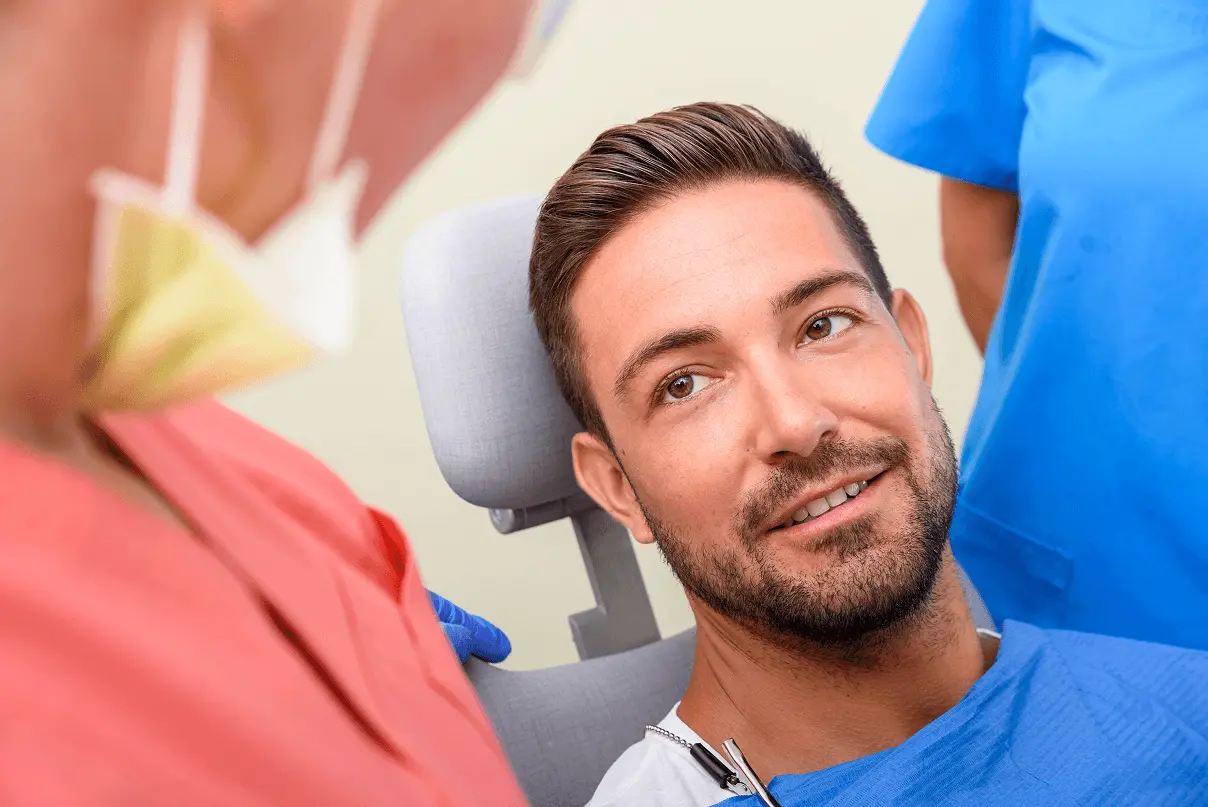Giovane uomo sorridente seduto sulla poltrona dentistica mentre parla con l'odontoiatra prima o dopo un trattamento dentale.