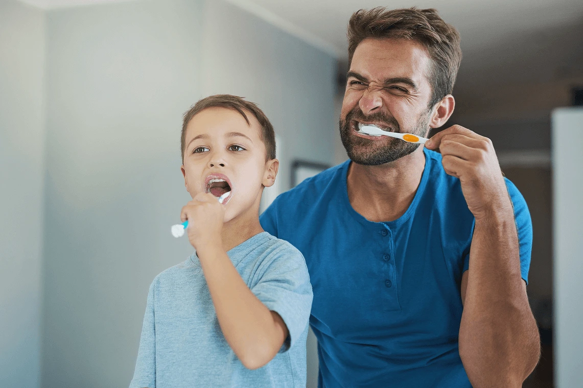 Padre e figlio che si lavano i denti insieme con lo spazzolino davanti allo specchio del bagno.