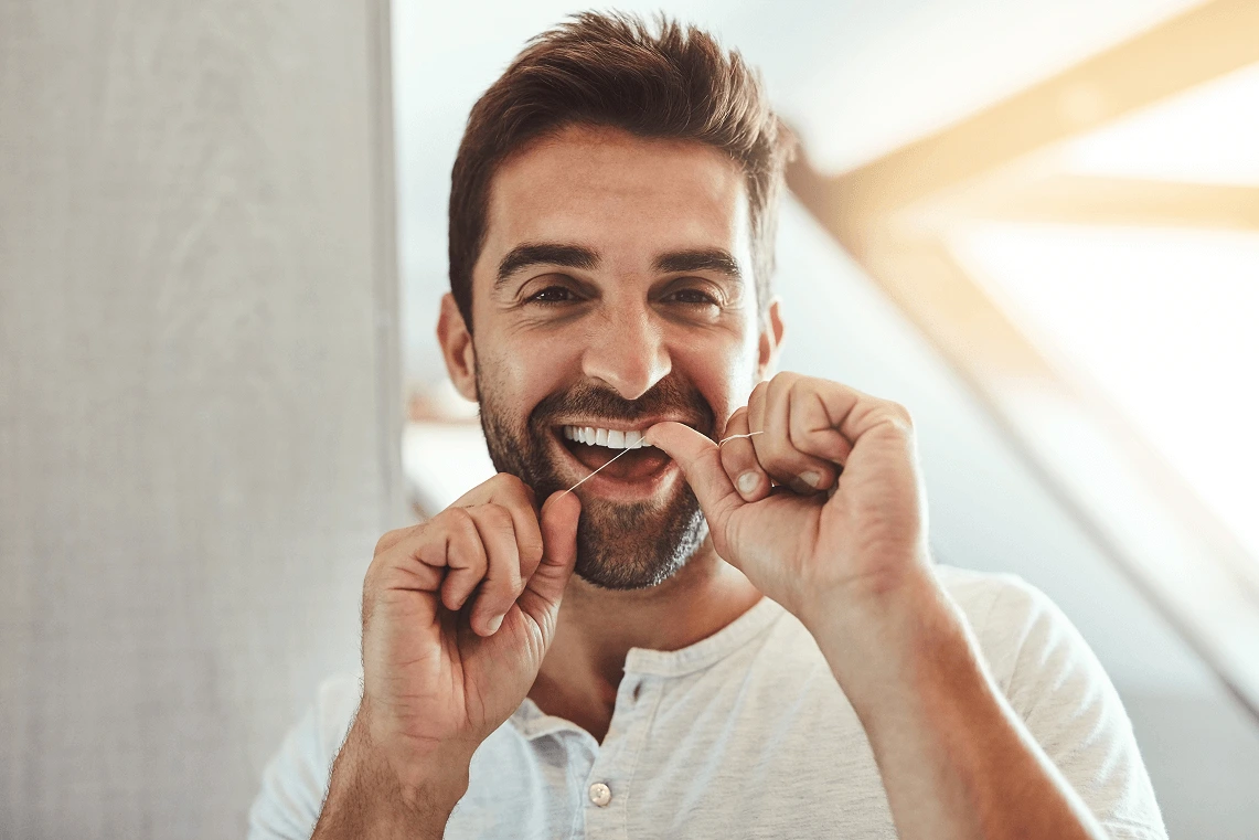 Uomo sorridente che usa il filo interdentale per la pulizia tra i denti.