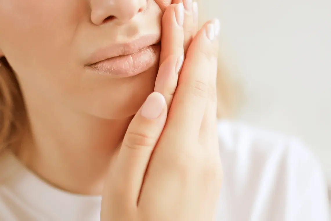 Primo piano del viso di una donna che si appoggia delicatamente la mano sulla guancia per un fastidio o dolore ai denti.