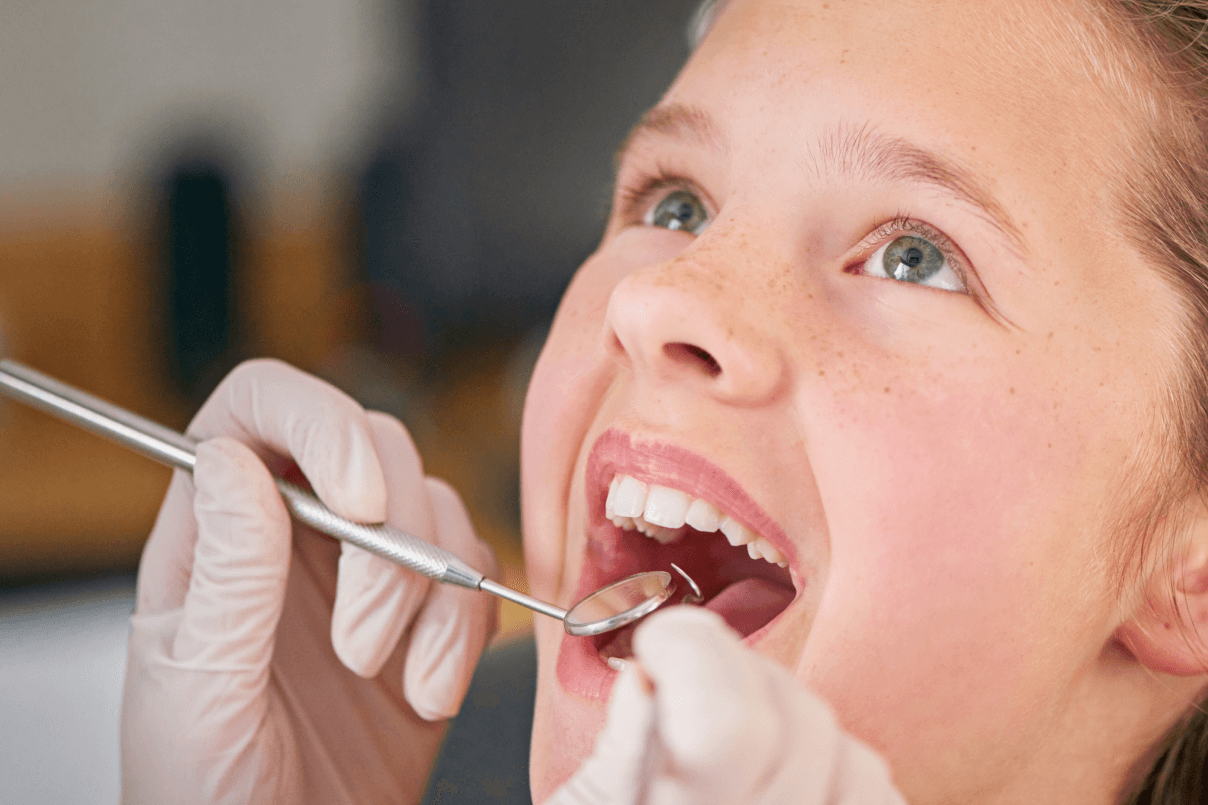 Primo piano del viso di una giovane ragazza con la bocca aperta mentre il dentista utilizza uno specchietto e una sonda per l'ispezione dei denti.