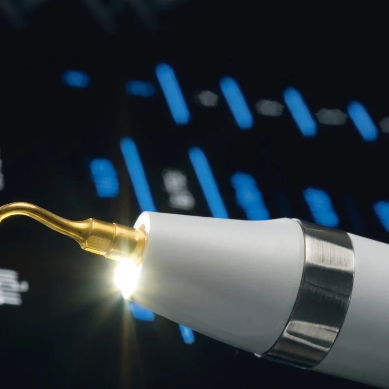 Dettaglio di un manipolo ultrasonico con punta dorata e luce LED integrata per la piezochirurgia dentale.