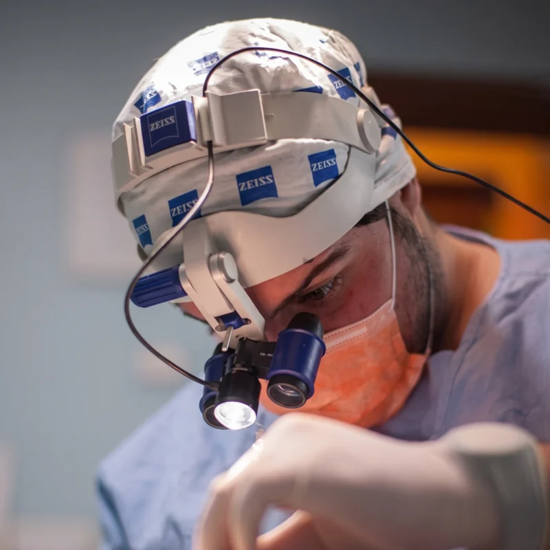 Dentista con occhialini ingranditori prismatici Zeiss e luce frontale concentrato durante un intervento chirurgico.