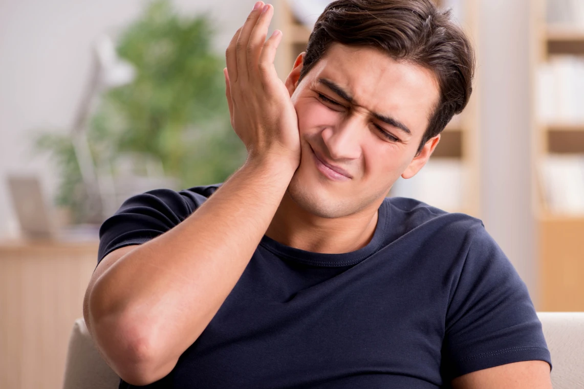 Uomo in maglietta blu scuro che si tiene la mano sulla guancia con un'espressione sofferta per il mal di denti.