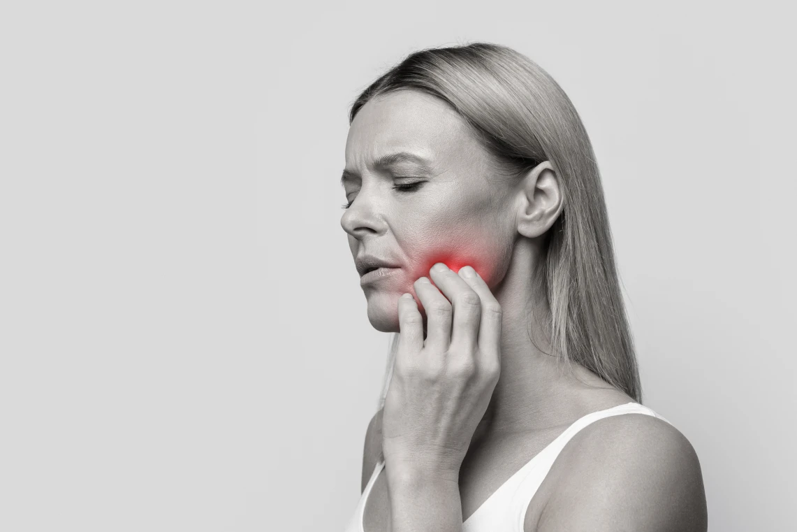 Foto in bianco e nero di una donna di profilo che si tocca la guancia con un'area rossa evidenziata a indicare forte dolore ai denti.